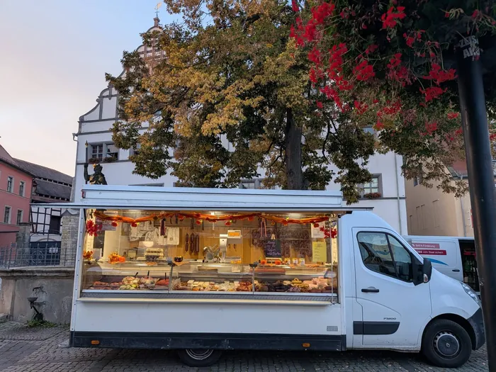 Verkaufswagen der Fleischerei Gallander mit geöffneter, beleuchteter Theke auf einem Marktplatz